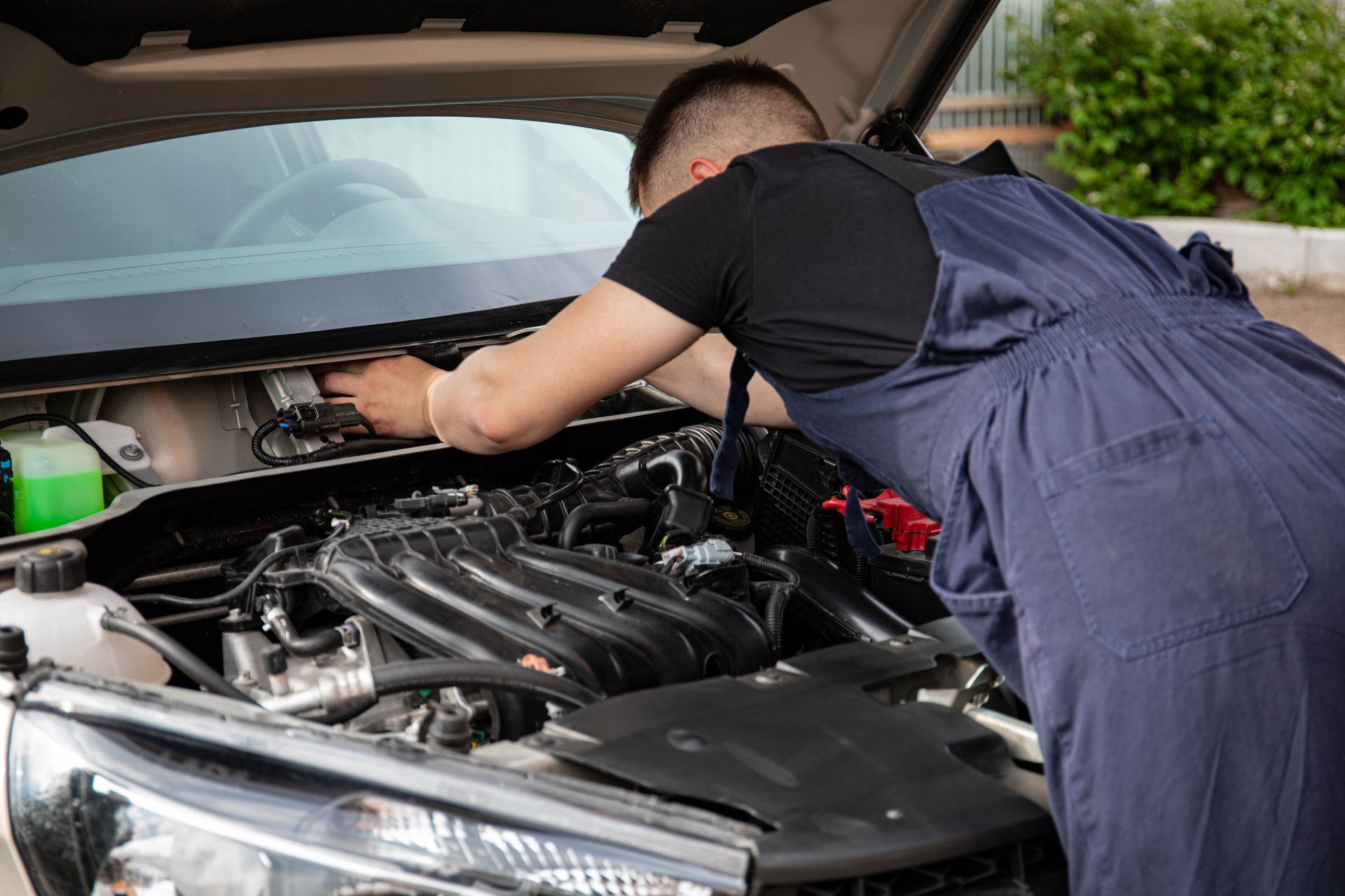 A mechanic performing maintenance work on a car's engine in an outdoor setting.